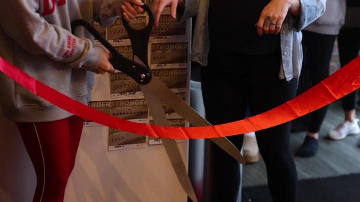 A large pair of scissors cutting a red ribbon. 