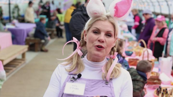 Chelsea O'Brien standing center frame wearing bunny ears for an interview about Easter on the Farm. 
