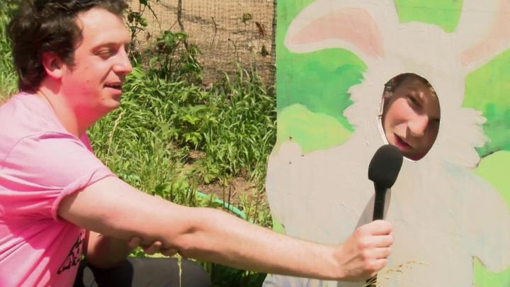 A man interviews a child through a rabbit cutout. 