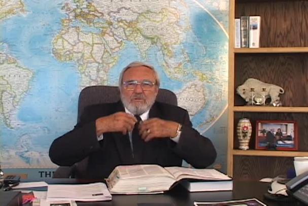 A man adjusts his tie sitting at a desk with a map behind him. 